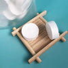 Two white compressed camping towels are displayed on a wooden tray next to a clear glass container.