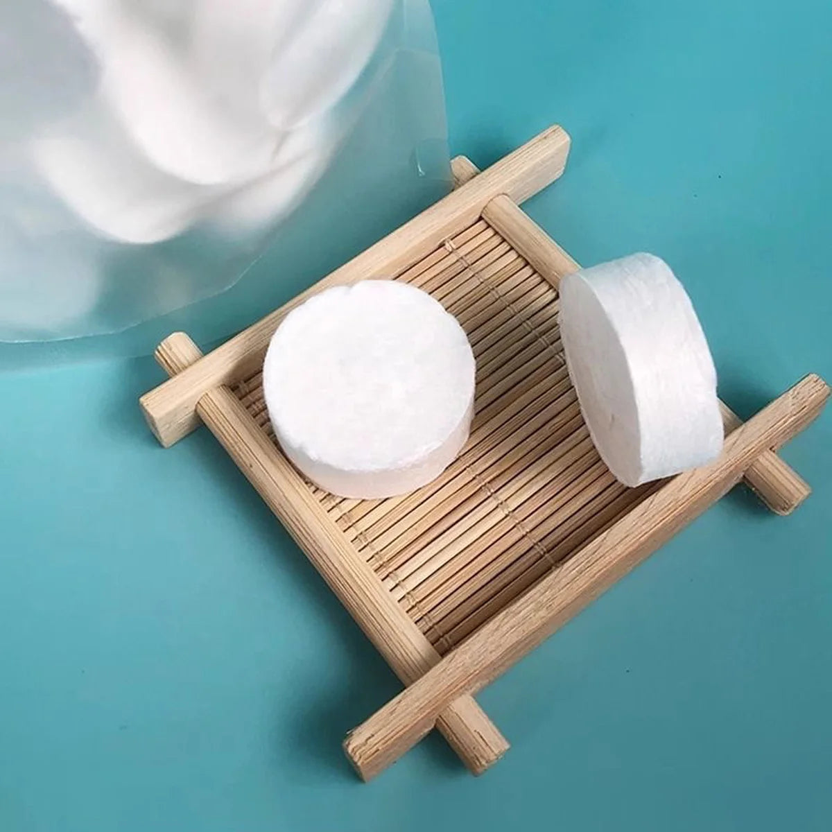 Two white compressed camping towels are displayed on a wooden tray next to a clear glass container.