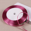 A roll of deep magenta satin ribbon on a white spool, ready for gift wrapping or crafts.