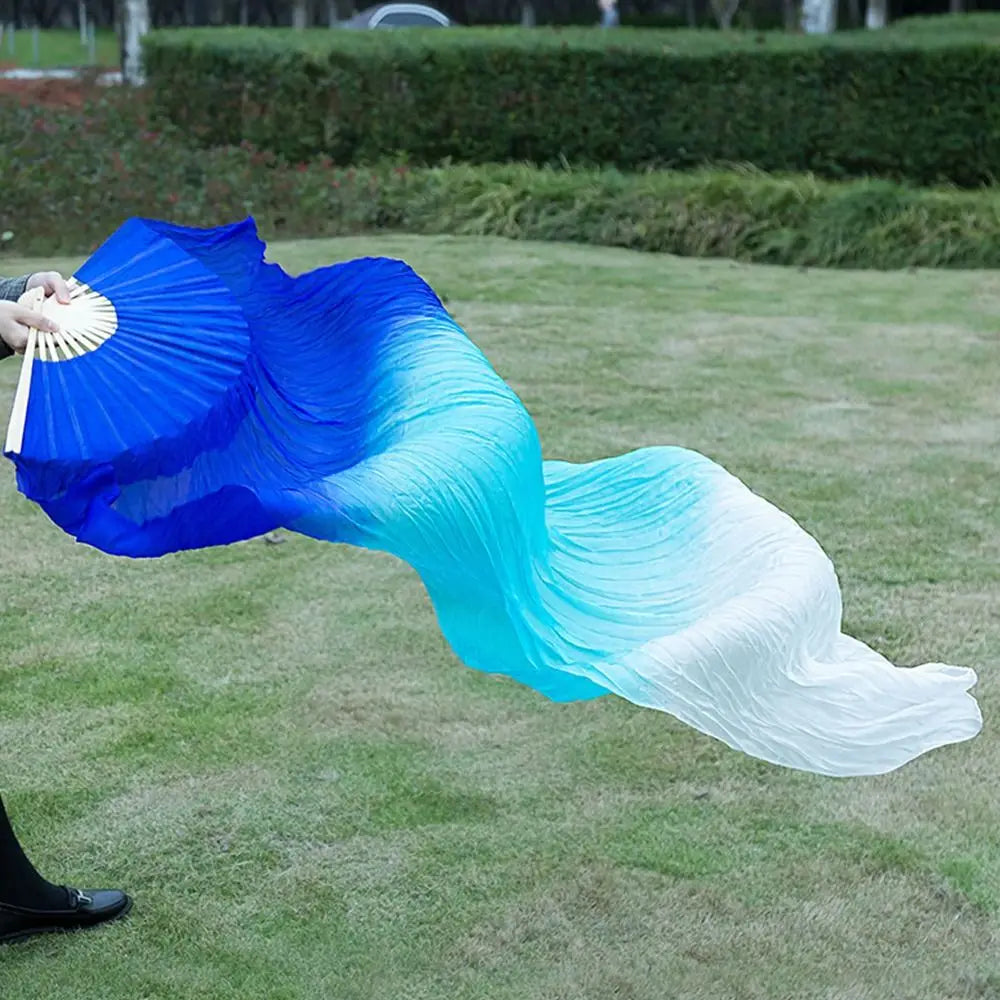 A silk ribbon dance fan showing a blue to white gradient, being held open on a grassy field.