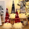 Three illuminated LED gnome Christmas decorations with warm glow and white fluffy beards displayed near a decorated Christmas