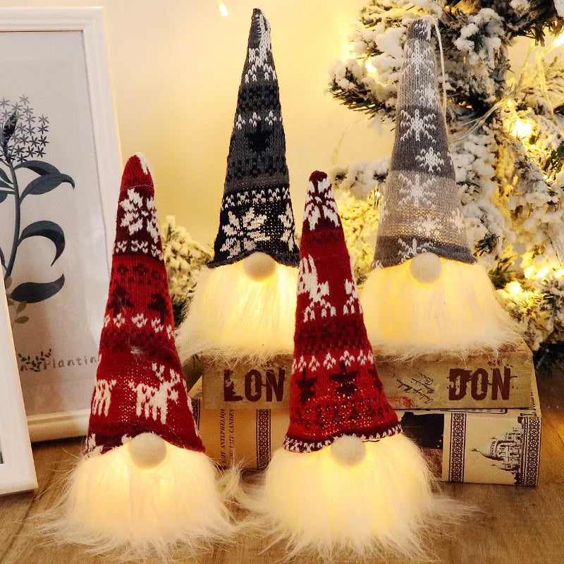 Three illuminated LED gnome Christmas decorations with warm glow and white fluffy beards displayed near a decorated Christmas