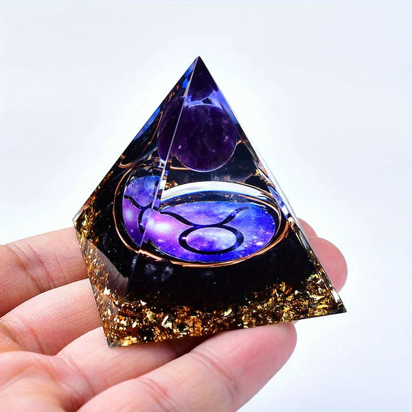 A dark pyramid crystal featuring purple and gold decorative elements held in a hand.