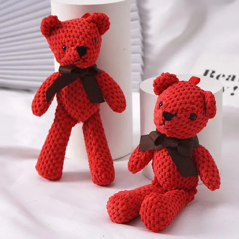 A handcrafted red yarn stuffed bear toy standing and sitting on a white cylindrical display stand.