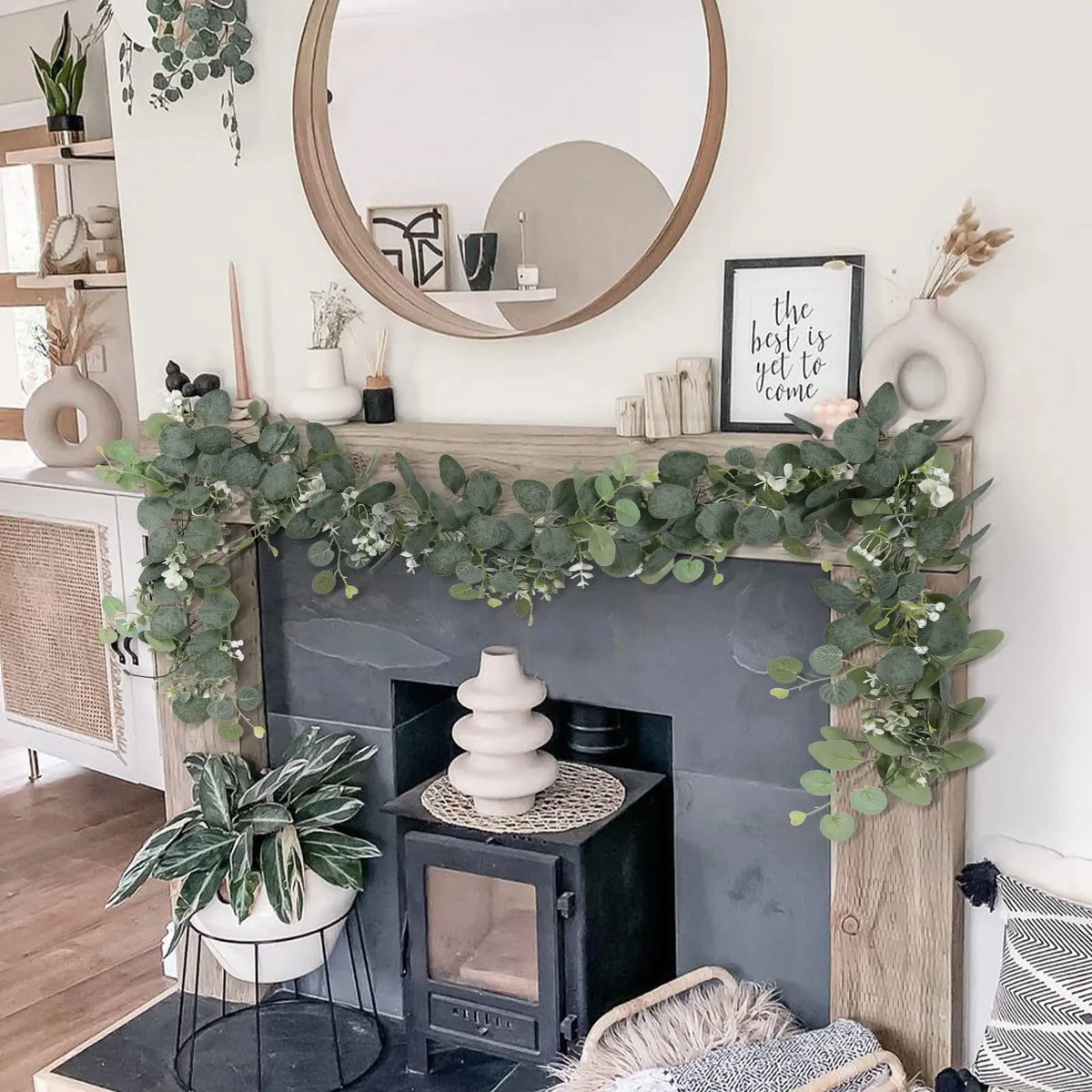 Artificial eucalyptus leaf garland draped across a fireplace mantel with potted plants and decor