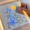يد ترسم قطة صفراء على لوحة رسم أكريليك مضيئة بأقلام، تضيء العمل الفني.