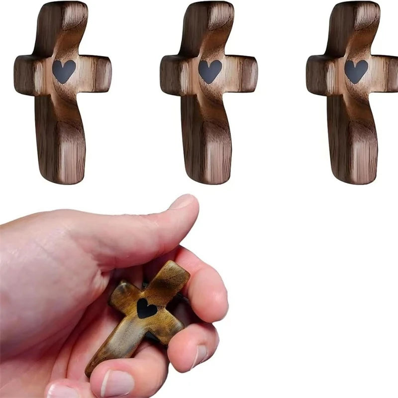 A hand holds a small wooden cross with an epoxy heart detail.