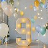 A glowing yellow LED marquee number 9 in a square frame sits on a wooden surface amidst balloons and string lights.