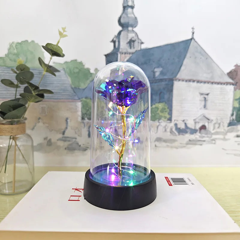 Rose de verre éternelle avec lumière LED, exposée sur une surface blanche devant un bâtiment historique.