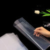 Una mano sostiene una hoja de carpeta plástica transparente con costura decorativa y una flor blanca, demostrando el producto