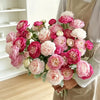 A lush bouquet of pink and white silk peonies arranged in a hand, held by a person wearing a beige apron.
