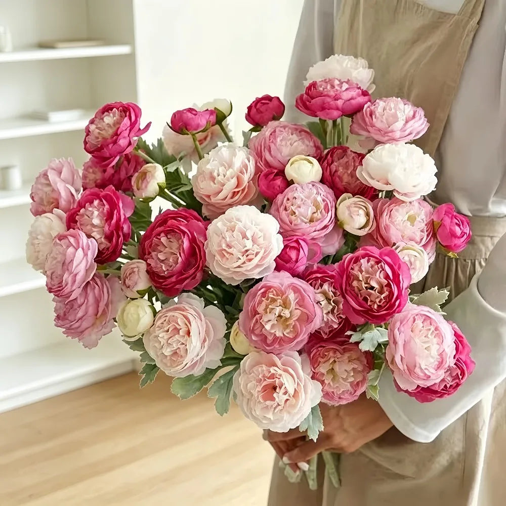 A lush bouquet of pink and white silk peonies arranged in a hand, held by a person wearing a beige apron.