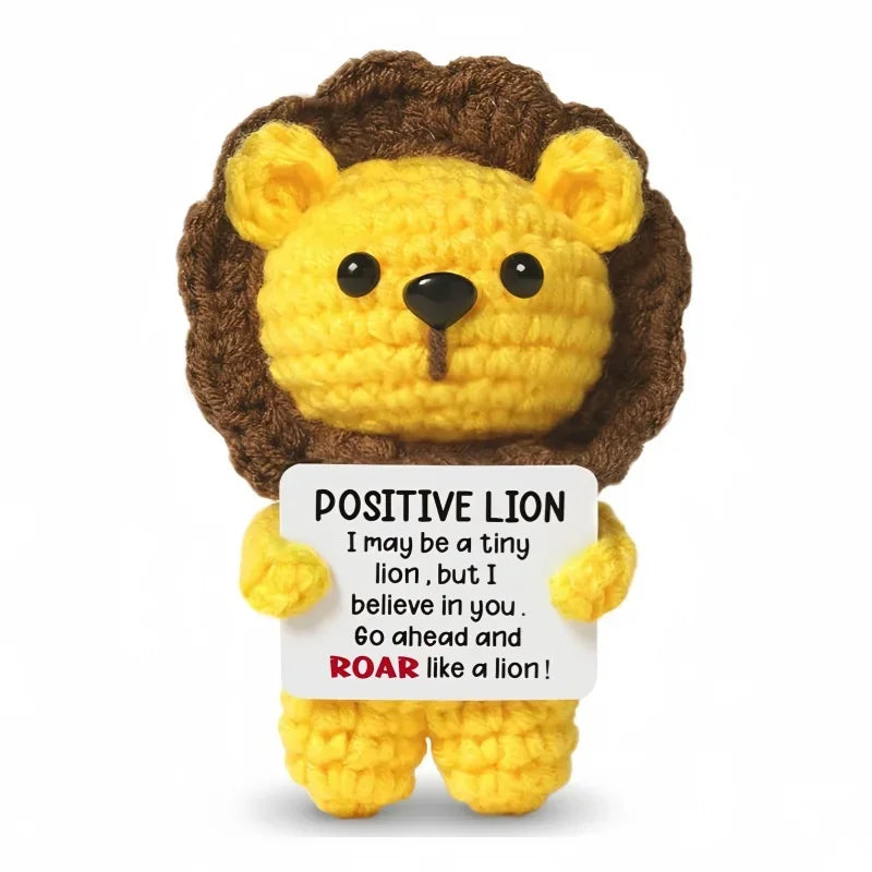 A yellow crocheted lion head and body with a brown mane, holding a card that says Positive Lion