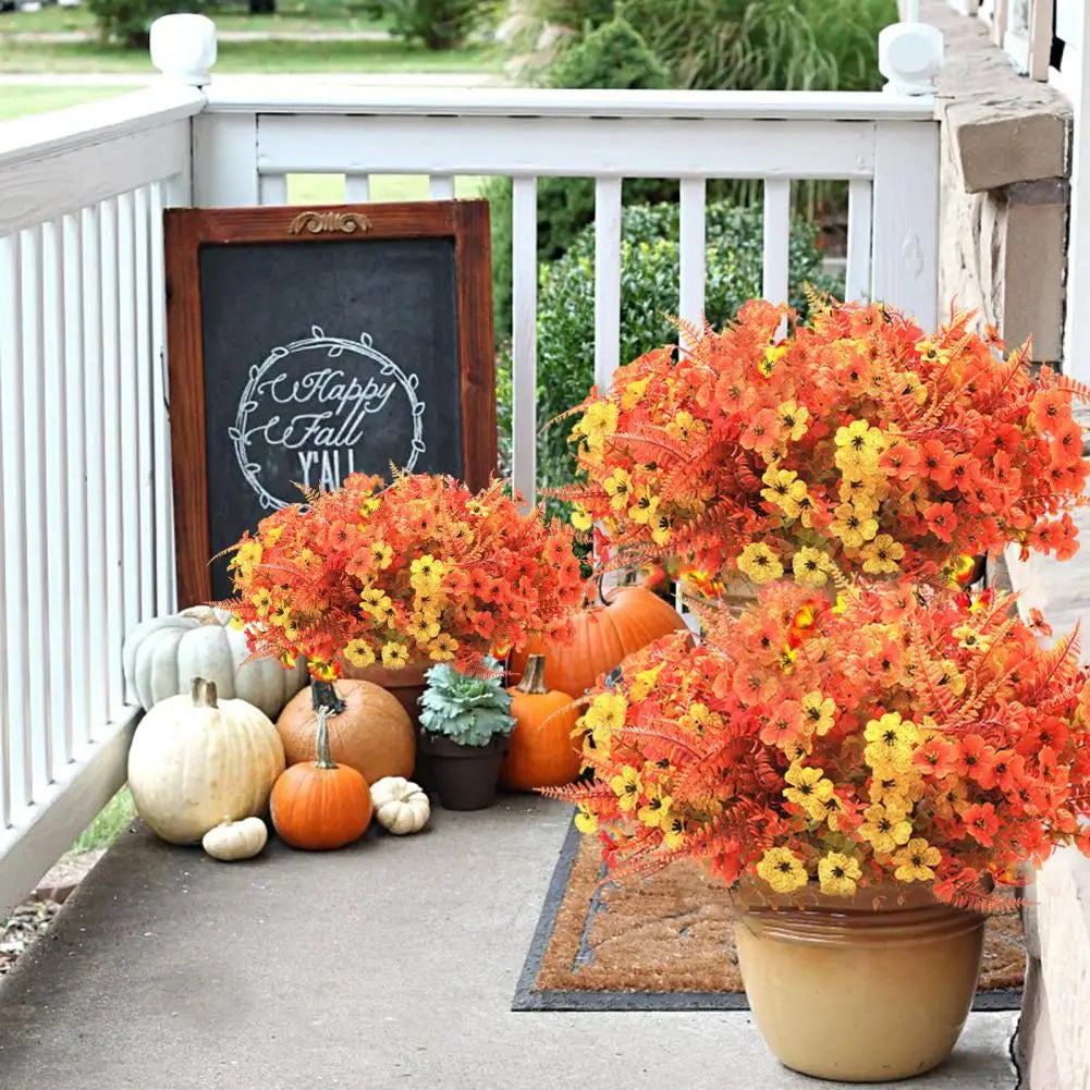 A vibrant display of artificial orange and yellow flowers in a pot sits on a porch railing next to pumpkins.