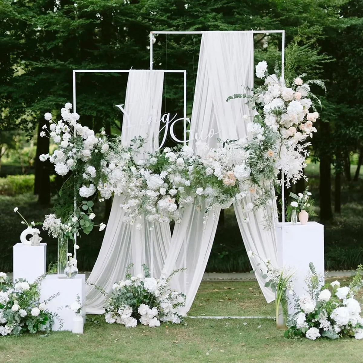 Elegant chiffon arch drapes in white and green floral arrangements for a wedding backdrop.