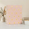 A pink laminated photo album with gold heart accents sits on a white surface.
