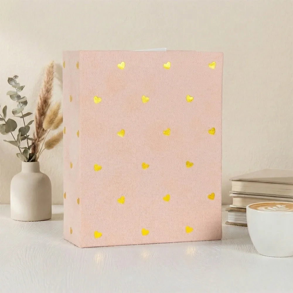 A pink laminated photo album with gold heart accents sits on a white surface.