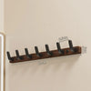 A walnut wood coat rack with eight hooks and a storage shelf mounted on a light wall.