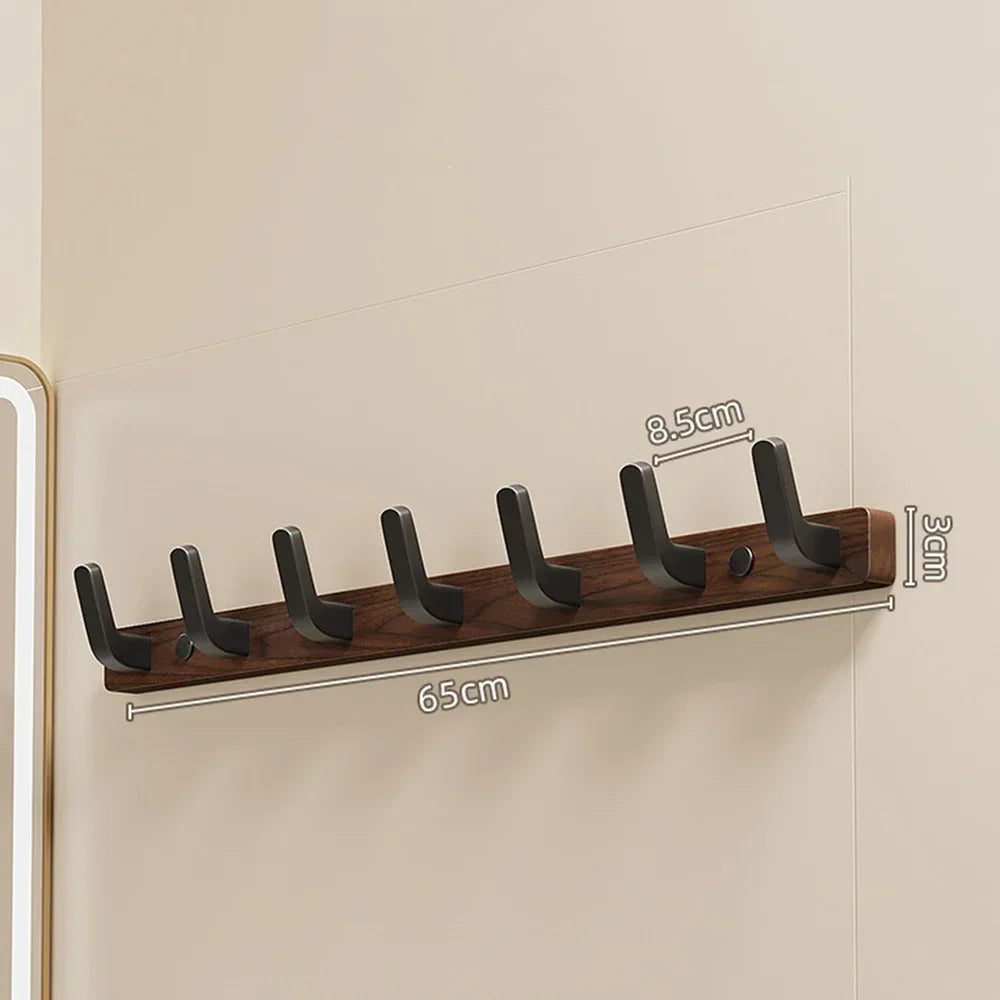 A walnut wood coat rack with eight hooks and a storage shelf mounted on a light wall.