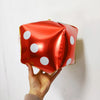 A red foil balloon shaped like a die with white polka dots being held by a hand.