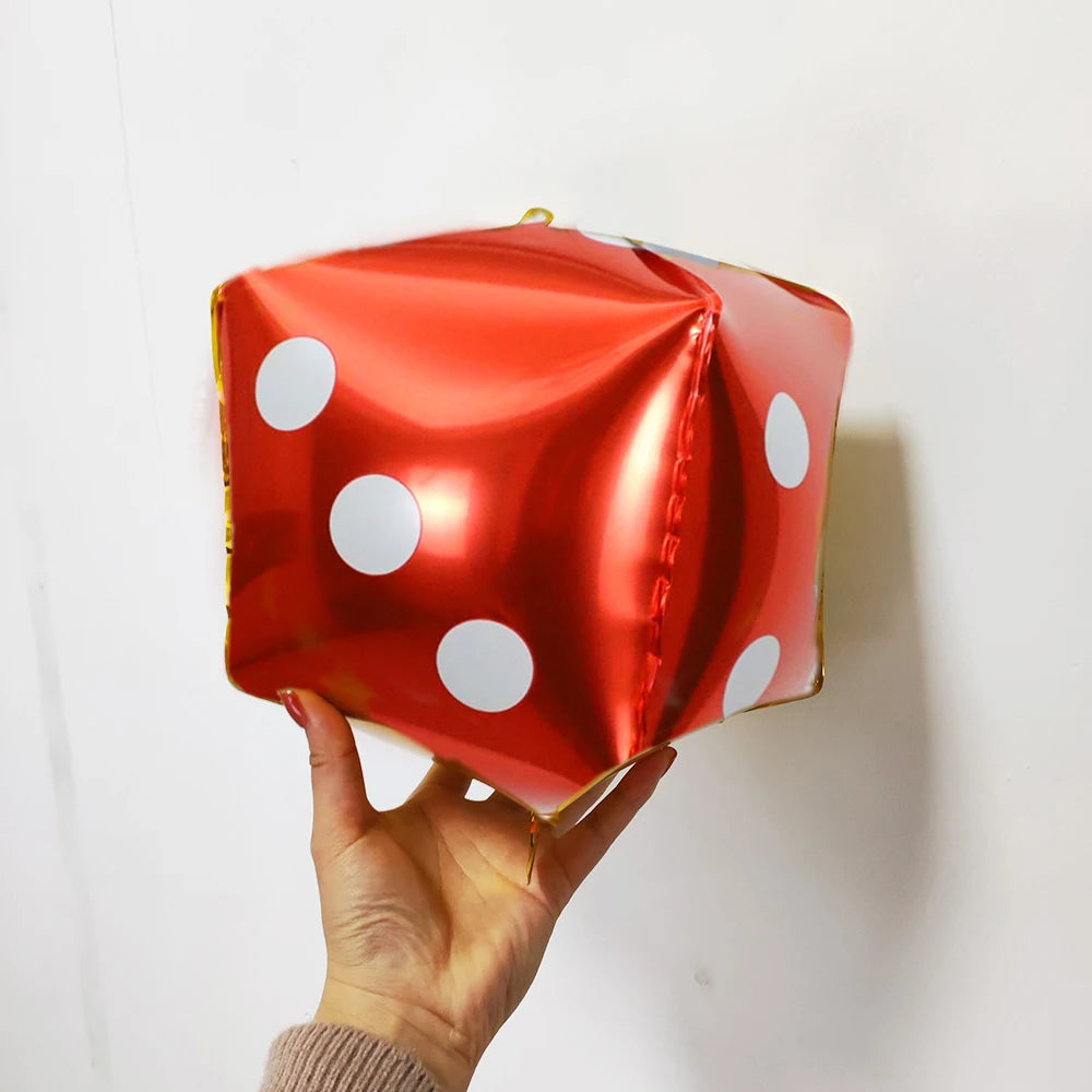 A red foil balloon shaped like a die with white polka dots being held by a hand.