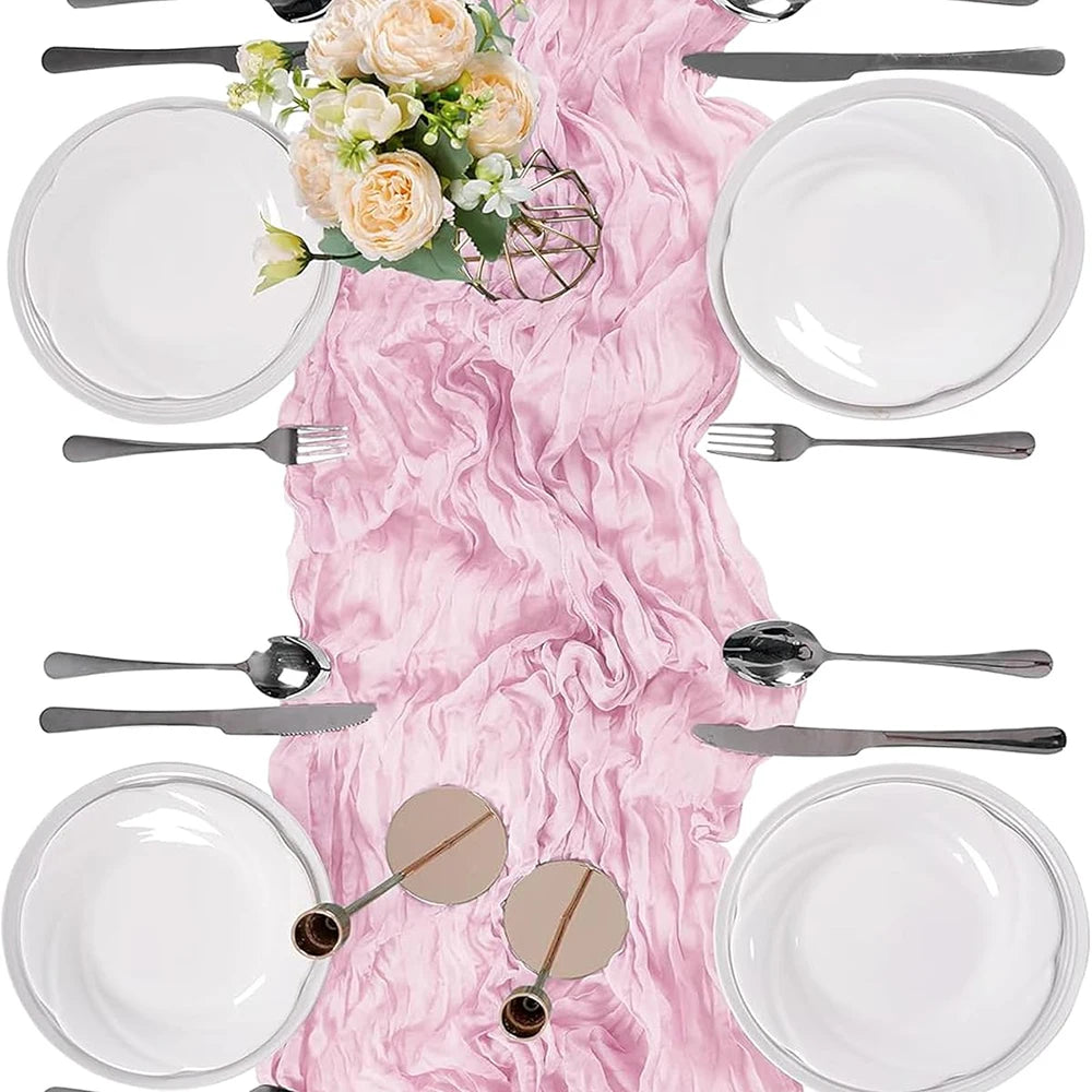 A rustic pink semi-sheer gauze table runner is displayed with a full place setting including plates, silverware, and a center