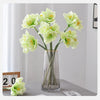 A vase holds several light green artificial clivia amaryllis flowers on a gray surface.