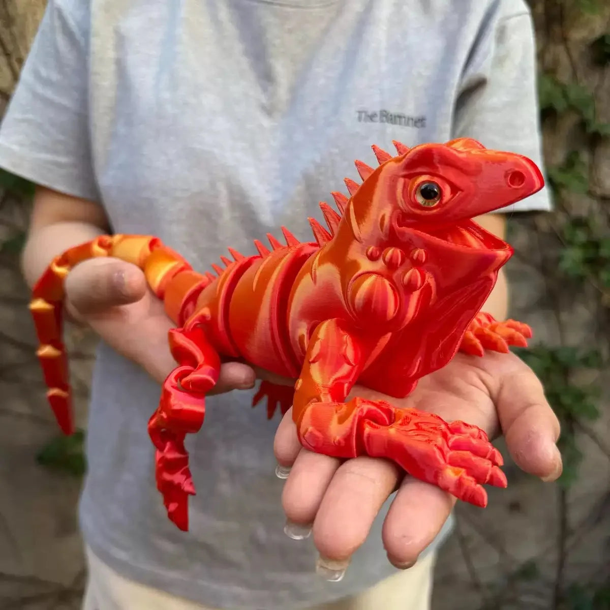 A hand holds an orange and red articulated 3D printed lizard figurine for home decor.