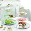 A three-tier plastic cupcake stand with green plates holding small pastries and cupcakes.
