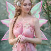 A woman wearing a pink fairy costume with butterfly wings and a flower crown, standing in a garden.