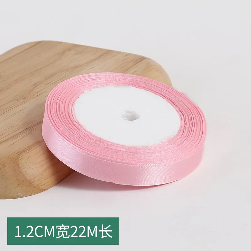 Roll of pink silk satin ribbon with a white center core on a wooden surface