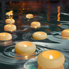 A close-up of glowing yellow LED floating sensor tealight candles reflecting on dark water.