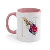 A pink ceramic coffee mug with a gold letter initial decorated with floral elements.