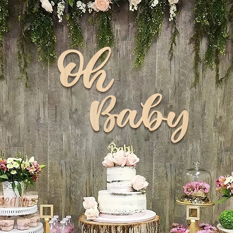Wooden sign spelling out Oh Baby with floral greenery and a tiered cake display