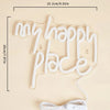 A white LED neon sign shaped like the words My Happy Place displayed on a light beige background.