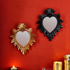 A pair of decorative wall mirrors shaped like hearts, one gold and one black, mounted on a red wall.