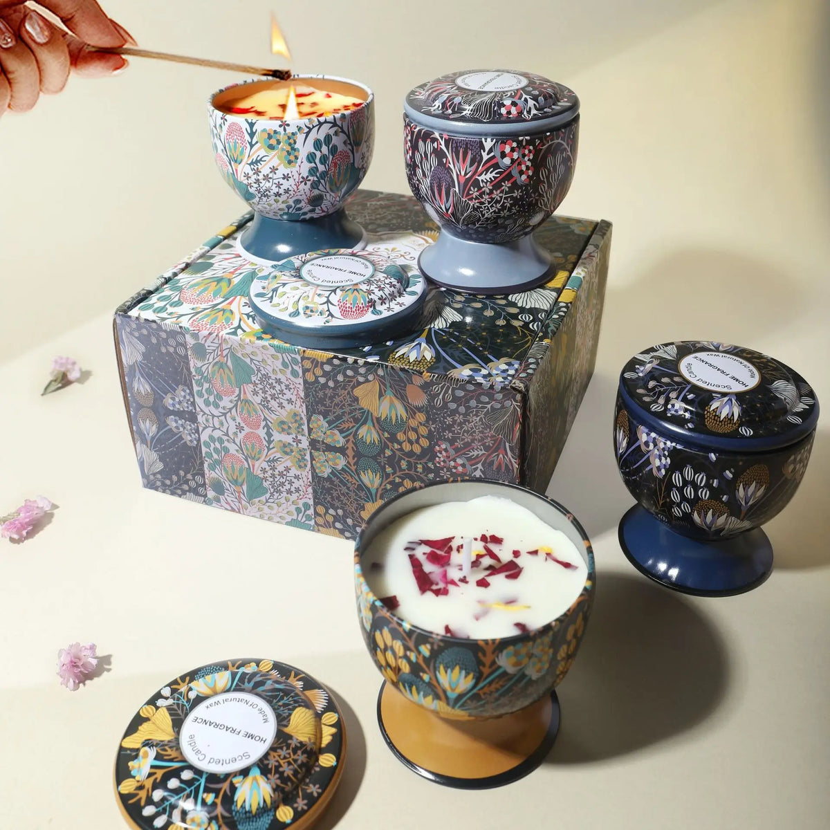 A gift set of soy wax aromatherapy candles in decorative tins and a lit candle being lit by a hand.