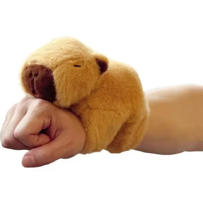 A hand is holding a small, golden-brown capybara animal wristband and ring.