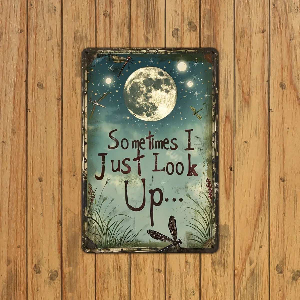 A vintage metal wall decor piece featuring a moon and dragonfly quote on a distressed plaque.