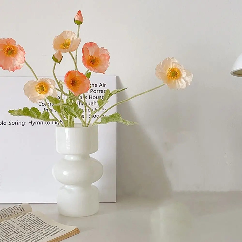 A white ceramic vase holds several delicate, handcrafted glass flowers with orange and pink petals.