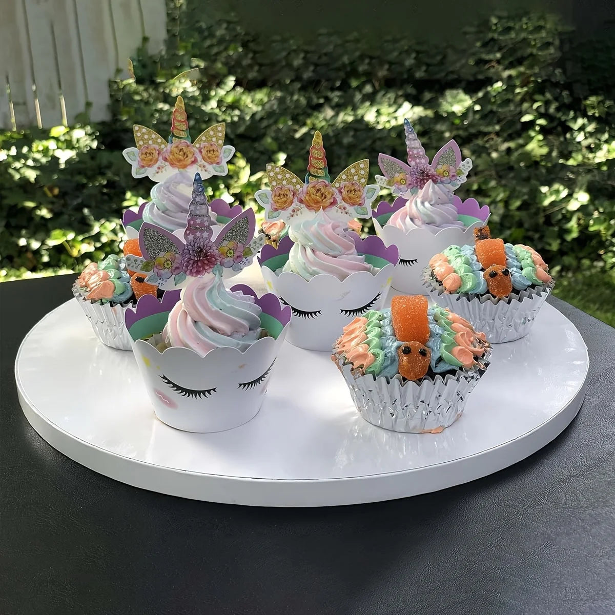 A display of colorful cupcakes decorated with floral and butterfly toppers arranged on a white cake board.