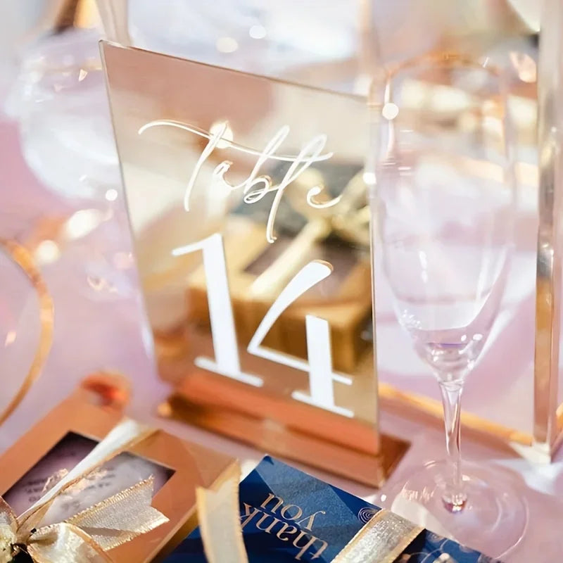 Elegant gold plated mirrored acrylic table numbers displayed on a pink background.