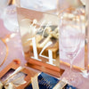 Elegant gold plated mirrored acrylic table numbers displayed on a pink background.