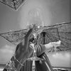 A hand holds a glass of sparkling drink against a backdrop of woven material and bright sunlight.