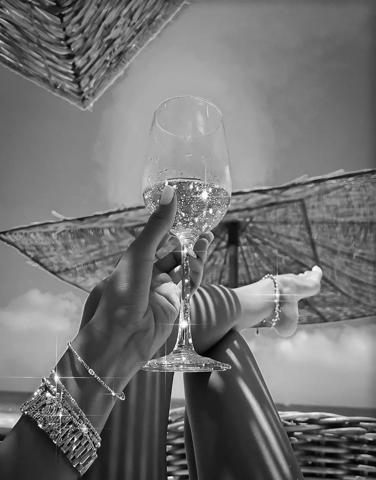 A hand holds a glass of sparkling drink against a backdrop of woven material and bright sunlight.