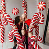 A group of people are holding red and white candy cane foil balloons for Christmas party decor.