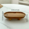 A light brown elliptical wooden storage tray with small feet, shown on a white marble surface.