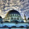 A dome-shaped Islamic mosque building with minarets under a cloudy sky.