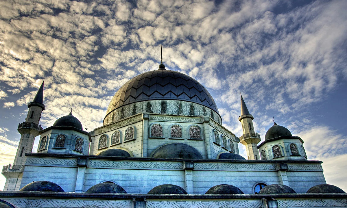 A dome-shaped Islamic mosque building with minarets under a cloudy sky.
