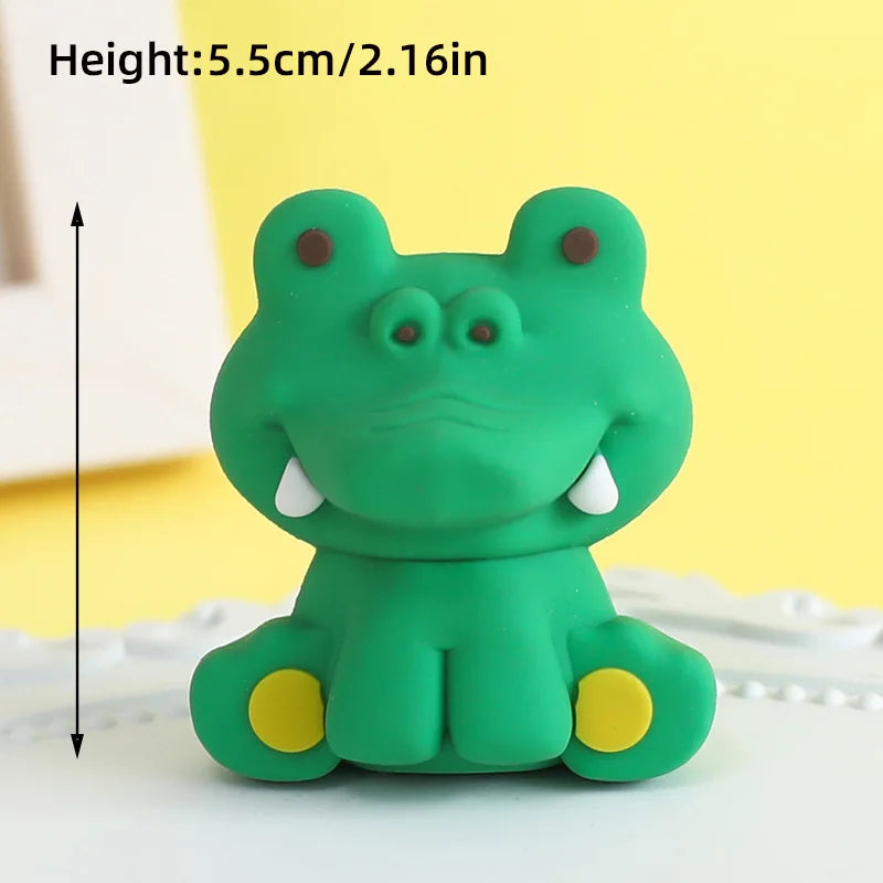 A green frog-shaped cake topper with brown eyes and yellow feet, shown against a white background.